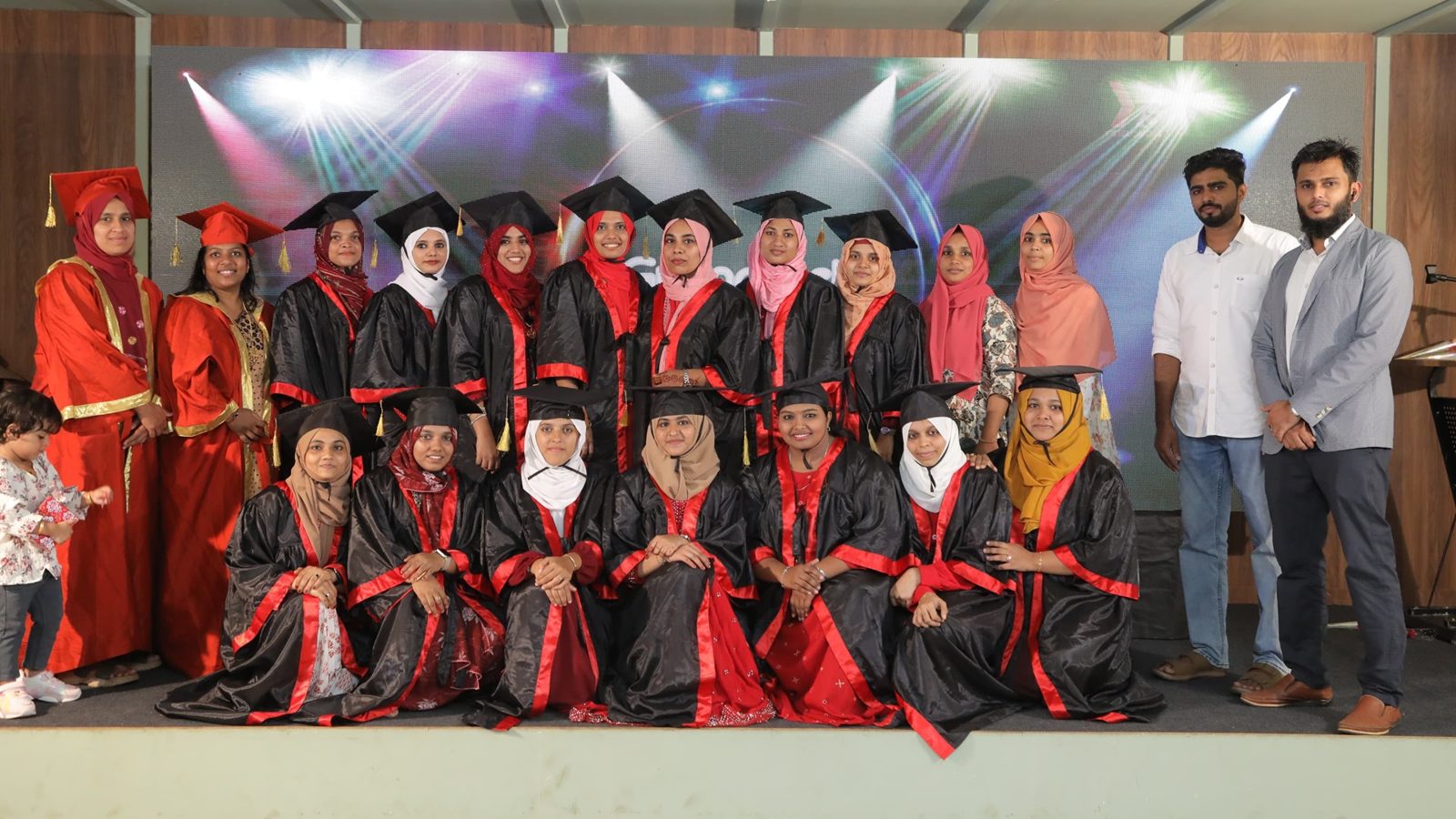 Trainee teachers in graduation gowns with faculty on stage
